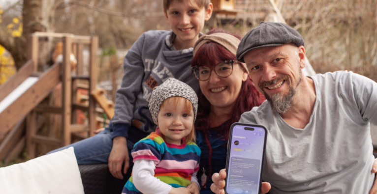 Hermann Rauschmayr und seine Familie sitzen im Garten. Er hält das Handy mit der Wunschlist App in die Kamera