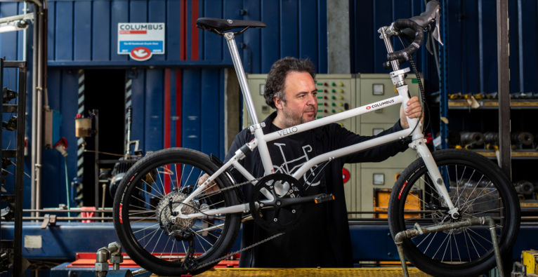 CEO und Chefdesigner Valentin Vodev präsentiert sein Vello Fahrrad in Mailand. Es steht auf einem Tisch und er hält es mit beiden Armen