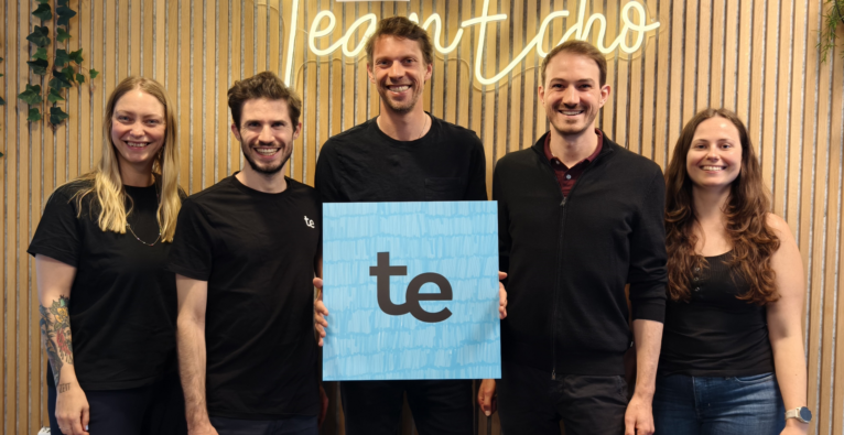 Die Gründer von teamEcho stehen vor einem Neon Schild mit der Aufschrift teamEcho und begrüßen Lukas Wieser