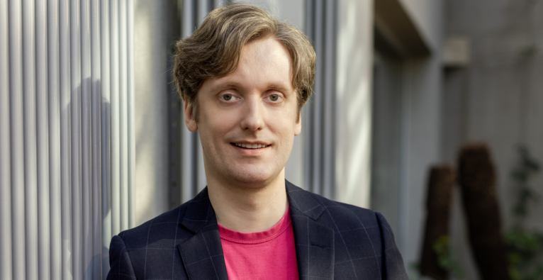 Mats Kuuskemaa lacht in die Kamera. Er hat blondes, lockiges Haar und ein pinkes Tshirt unter seinem schwarzen Blazer an. (c) e-Residency